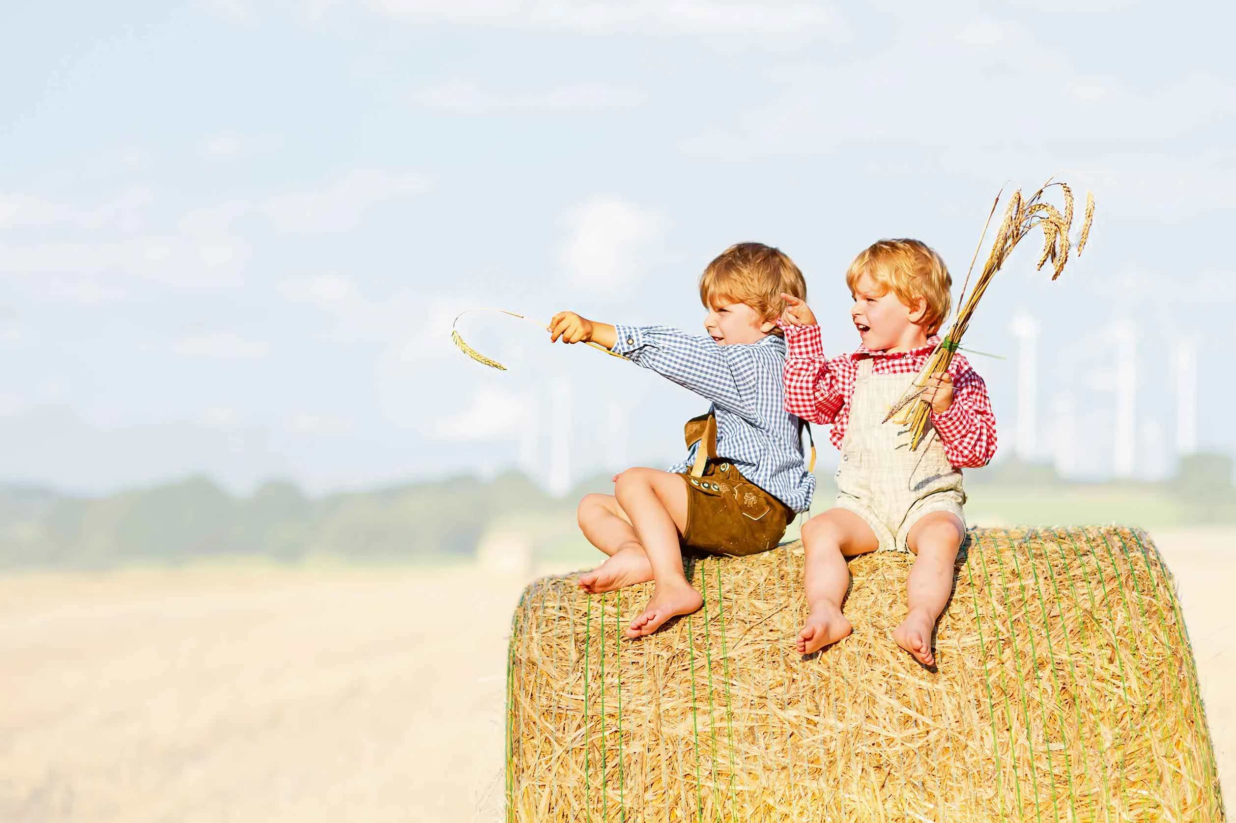 Kinder die an einem warmen sonnigen Tag auf einem Strohballen sitzen und spielen