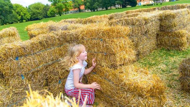 Kleines Mädchen dass hinter Strohbündeln verstecken spielt