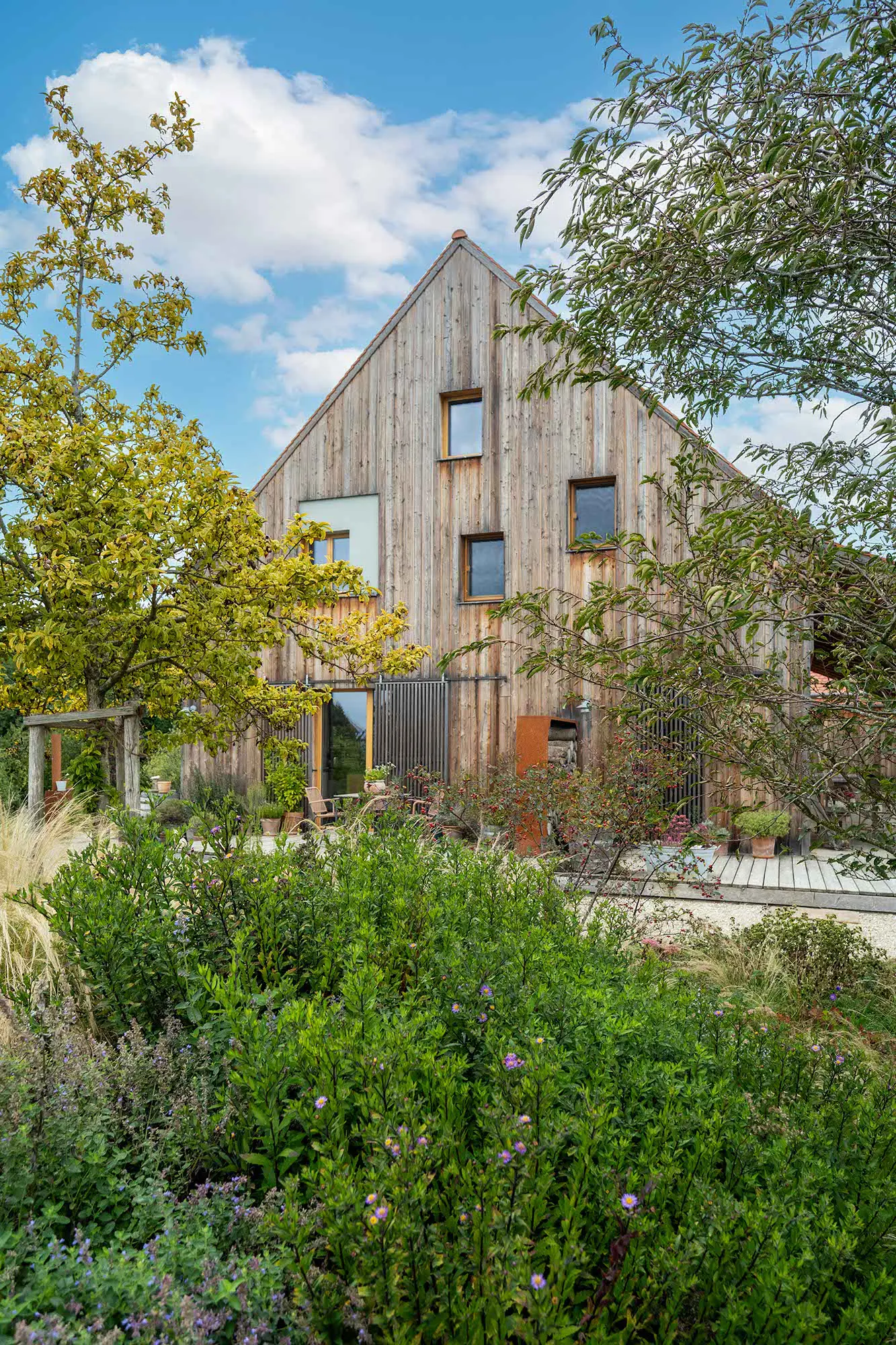 erneut das mit Holz beschichtete Haus, die Seite auf der man das Haus sieht zeigt viele unsymetrissche kleine Fenster und die Terasse