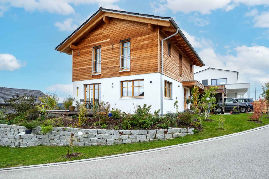 Weiß/ Holzbraun beschichtetes Haus mit vielen Fenstern, einem Vorgarten und Garage