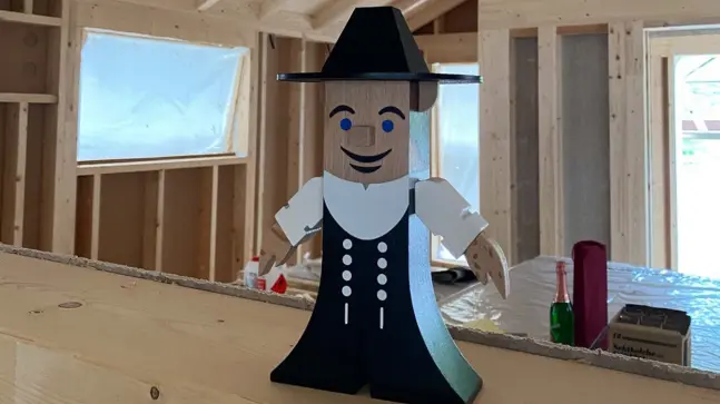 Holzfigur mit Grünem Kleid und Hexenhut in einem Holzhaus