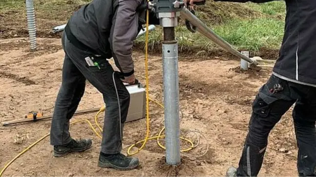 eine Nahaufnahme einer Einrichtung eines Hausanschlusskastens, der von 2 Bauarbeitern in Schwarzer Arbeitskleidung arbeiten.