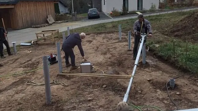 Baustelle mit Quadratischer Erdfläche. Auf dieser Erdfäche sind drei Bauarbeiter zu sehen die einen Hausanschlusskasten auf der Erdfläche einrichten.