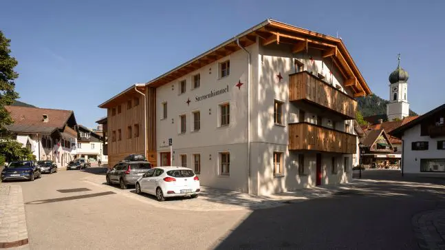 Großes Haus mit mehreren Balkonen und vielen Fenstern, Aufschrift Sternenhimmel mit Roten Sternsymbolen auf Weißer Hauswand , neben dem Haus sind